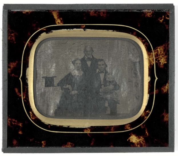 Schwarz-weiß-Foto eines Mannes im Anzug und einer Frau in unbekannter Kleidung vor einem Fernseher mit ernsten Gesichtern.