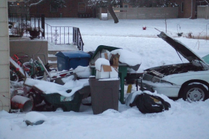 Eine Außenansicht mit Müll in der Mitte, ein Auto auf der rechten Seite, Treppen auf der linken Seite, Bäume oben und Eis auf dem Boden.