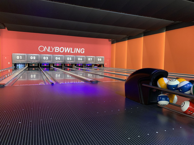 Eine Bowlingbahn mit Bowlingkugeln auf der rechten Seite, Bowlingkegel in der Mitte und einer textbedeckten Wand im Hintergrund, mit der Decke oben.