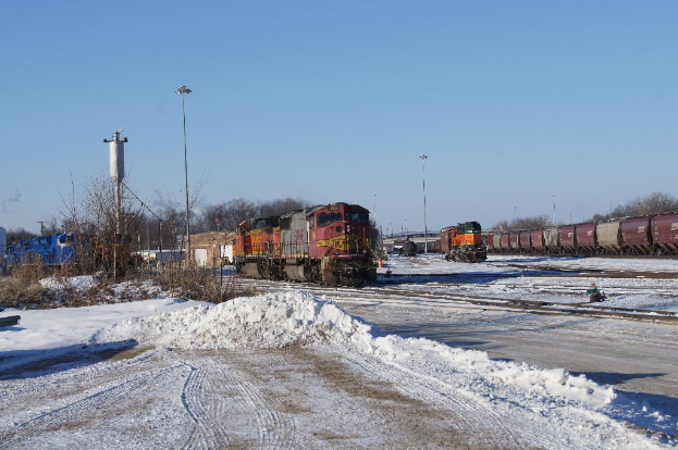 Eine Lokomotive vorne mit einem Waggon auf der rechten Seite, auf den Schienen geparkt mit Schnee am Boden, trockenen Bäumen und einem Strommast im Hintergrund.