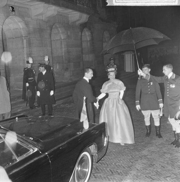 Schwarzes und weißes Foto von Queen Elizabeth II und Prinz Philip, Herzog von Edinburgh, bei der Ankunft in Buckingham Palace in formeller Kleidung, wobei die Queen einen Strauß hält und der Herzog einen Schirm hält, vor einem Gebäude mit Bögen und Säulen.