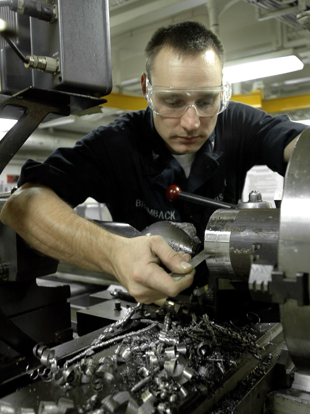 Ein Fräser mit Brille bedient eine Maschine in einer gut beleuchteten Fabrikumgebung.