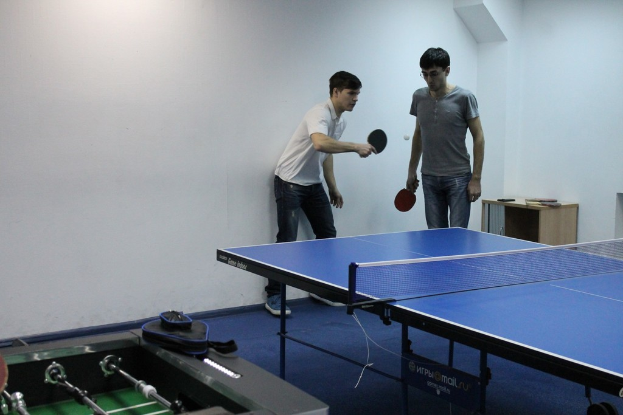 Zwei Personen spielen Tischtennis, wobei eine Person den Ball über das Netz zur anderen schlägt.