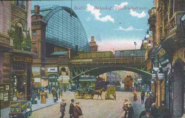 Eine sepiafarbene Postkarte zeigt eine belebte Berliner Straßen Szene mit Fußgängern, Pferdewagen, Gebäuden, Laternen, einer Brücke und einem bewölkten Himmel, mit Text oben.