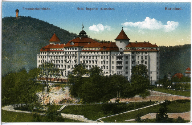 Alte Postkarte des Hotel Imperial in Karlsbad, Deutschland, zeigt ein großes Gebäude mit Fenstern umgeben von Bäumen, Pflanzen, Gras, einem Pfad, einer Baumgruppe, Hügeln und einem bewölkten Himmel, mit Text oben.