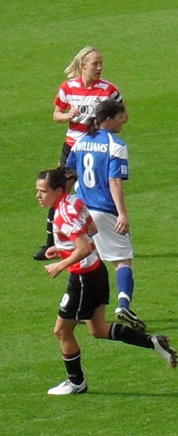 Drei Frauen in Sportuniformen spielen Fußball auf einem grünen Feld.