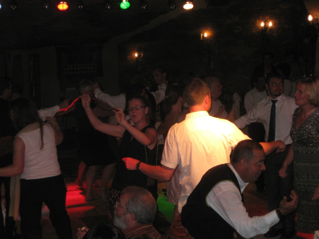 Eine lebendige Partyszene mit tanzenden Menschen auf dem Boden unter verschiedenen farbigen Lichtern in einem dunklen Raum.