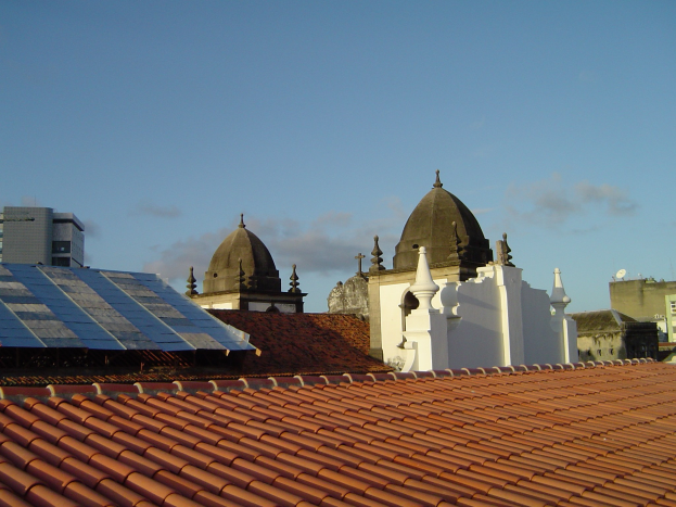 Eine Stadtansicht mit mehreren Gebäuden im Vordergrund, einem blauen Himmel im Hintergrund und Solarpanelen auf dem Dach eines Gebäudes.